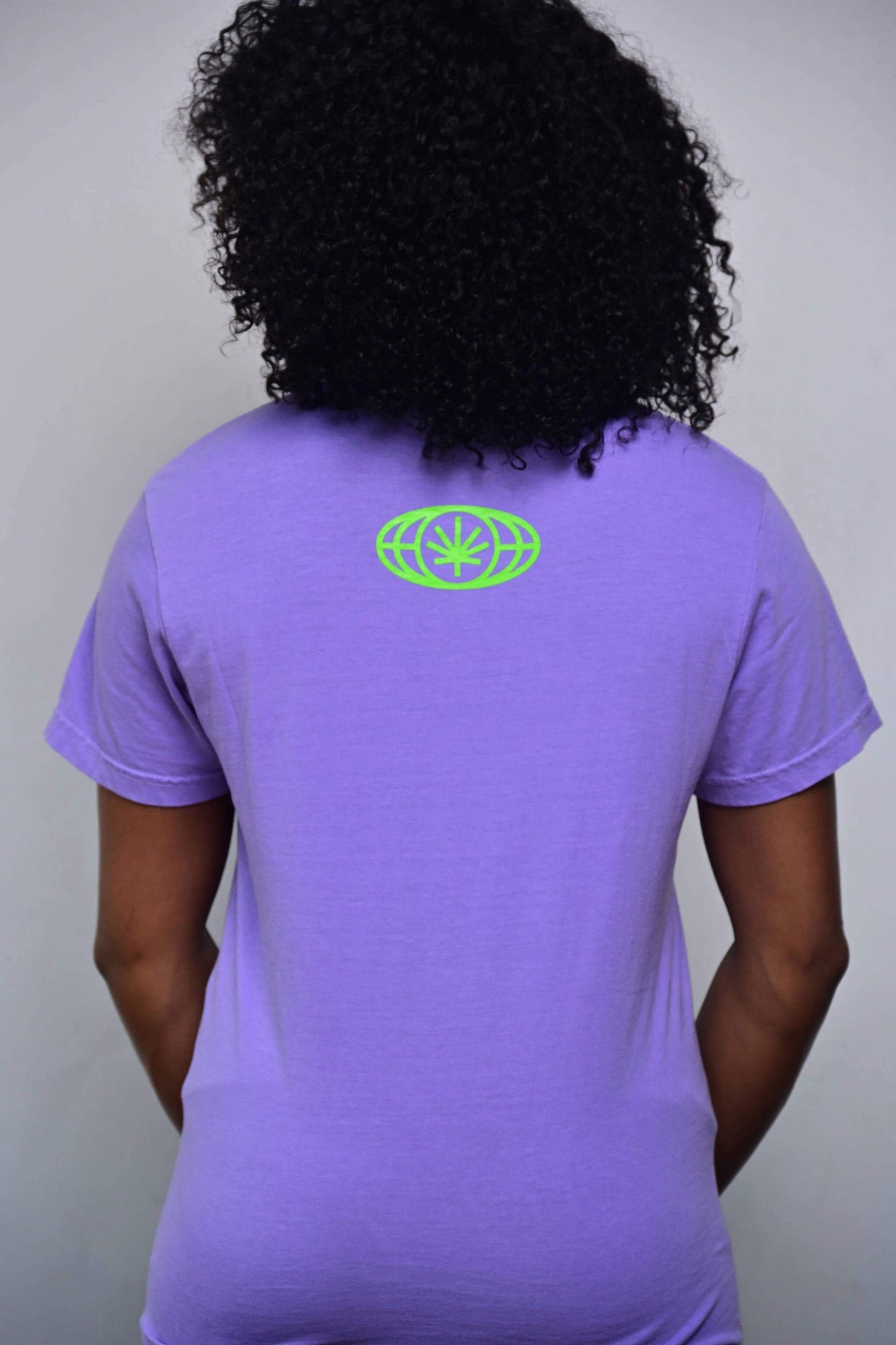 Violet tee with small acid green VYLIN globe icon centered ~3 in below back neckline (back, on-model)