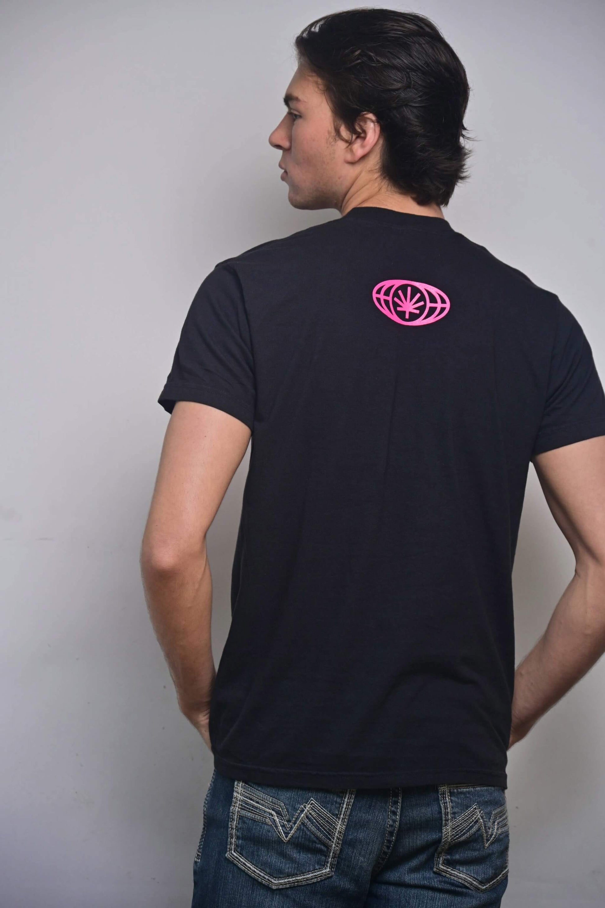 Black tee with small hot pink VYLIN globe icon centered ~3 in below back neckline (back, on-model)