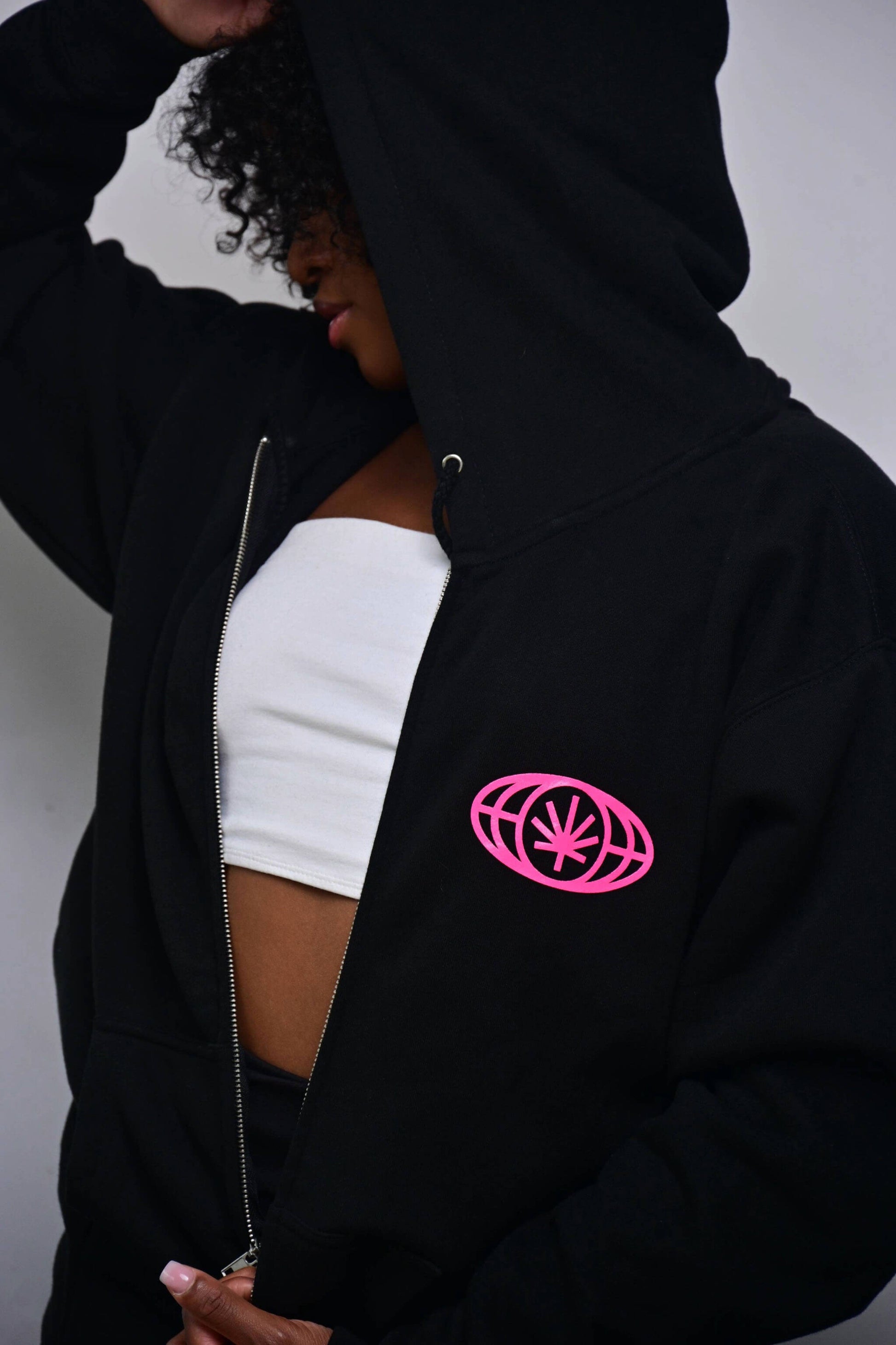 Black zip hoodie with small hot pink VYLIN globe icon at left chest (front, on-model)