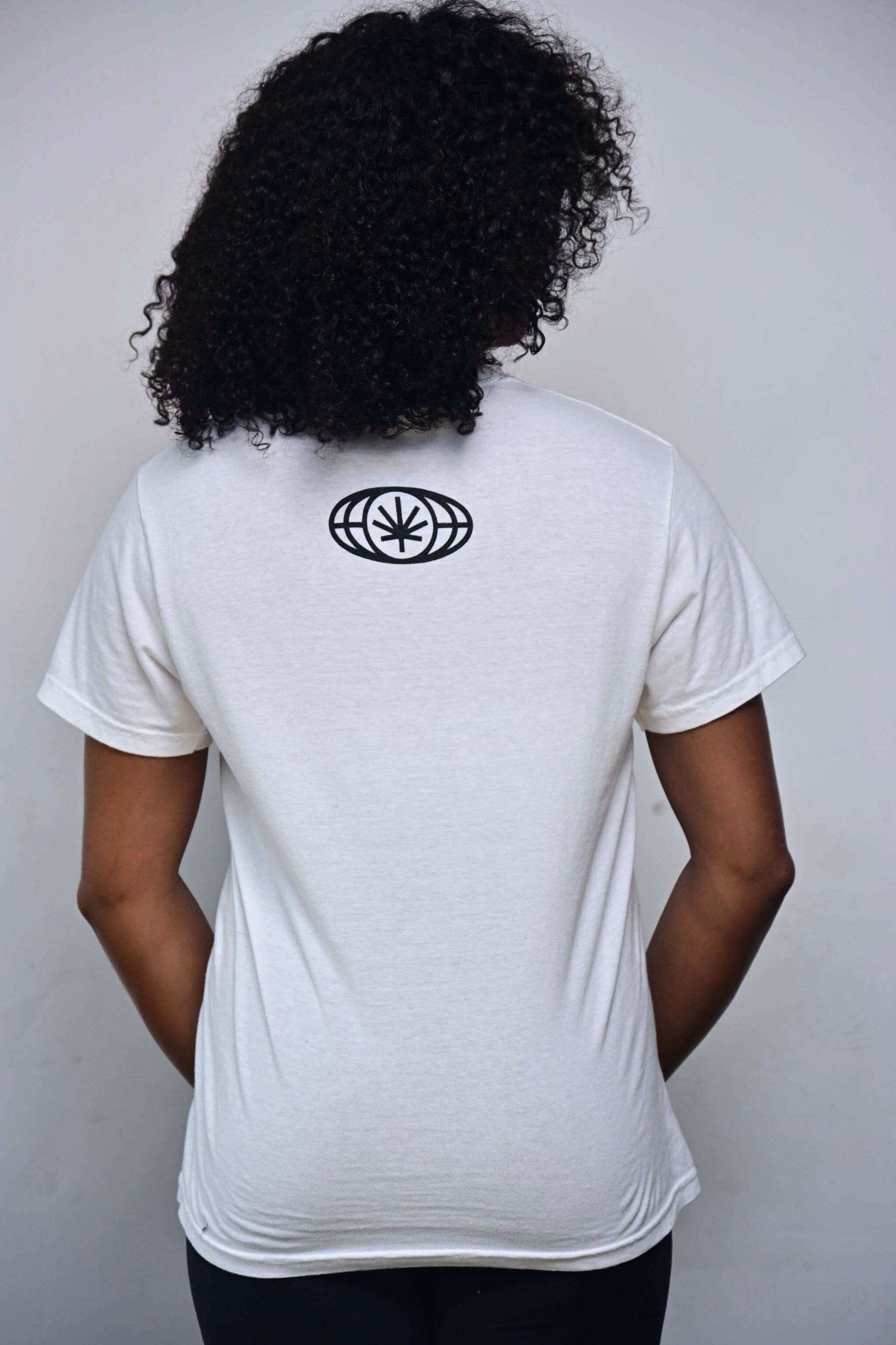 White tee with small VYLIN globe icon centered ~3 in below back neckline (back, on-model)