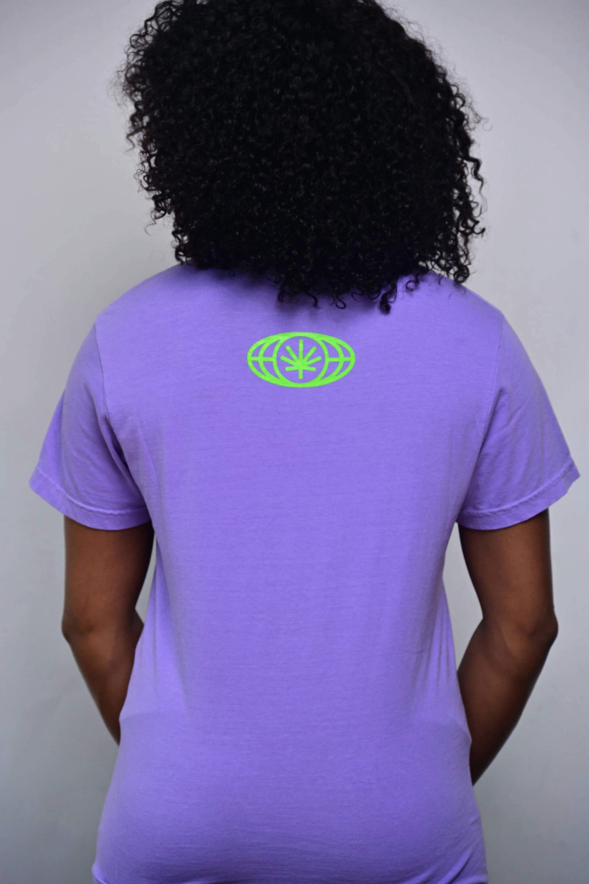 Violet tee with small acid green VYLIN globe icon centered ~3 in below back neckline (back, on-model)