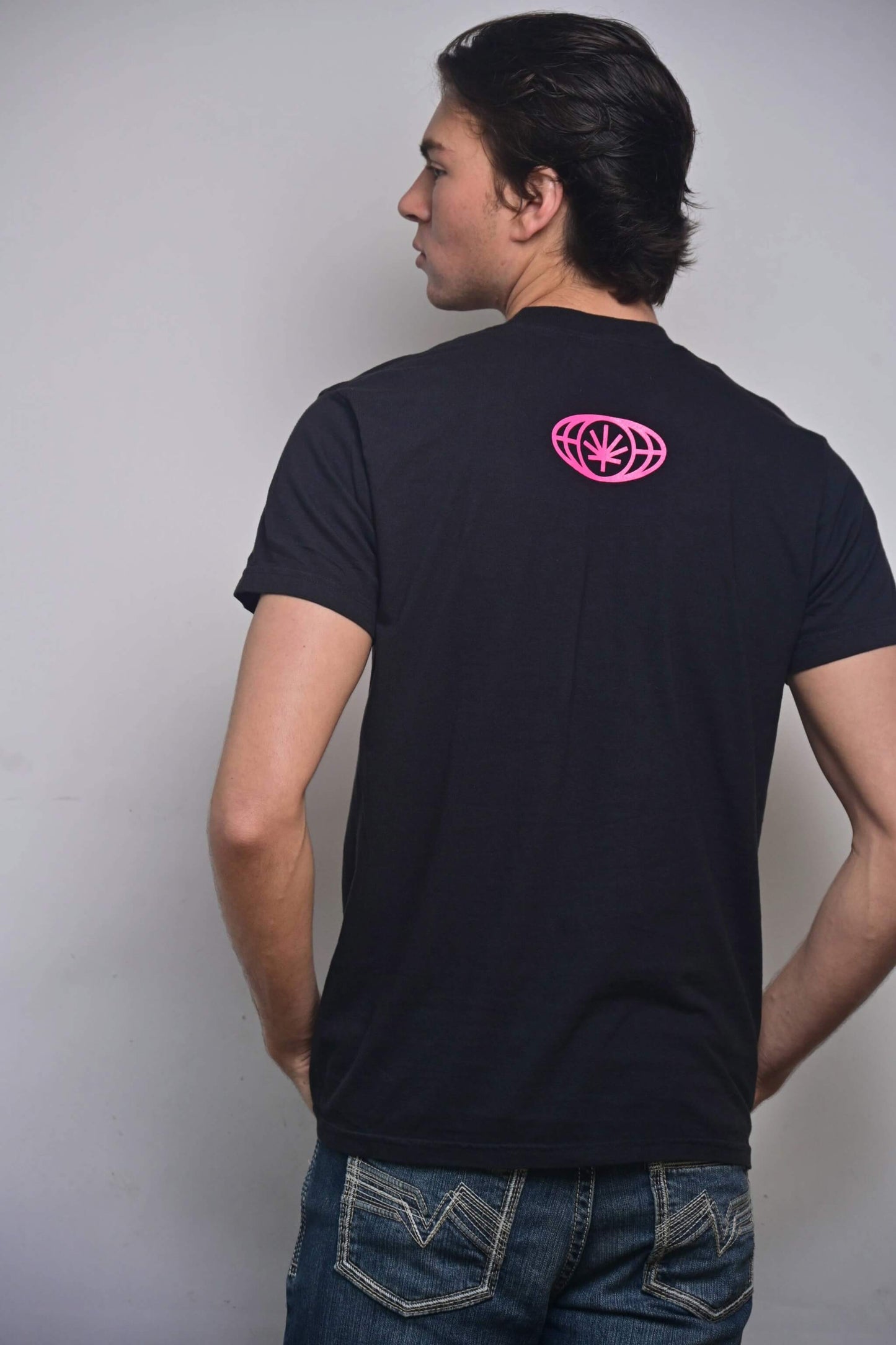 Black tee with small hot pink VYLIN globe icon centered ~3 in below back neckline (back, on-model)